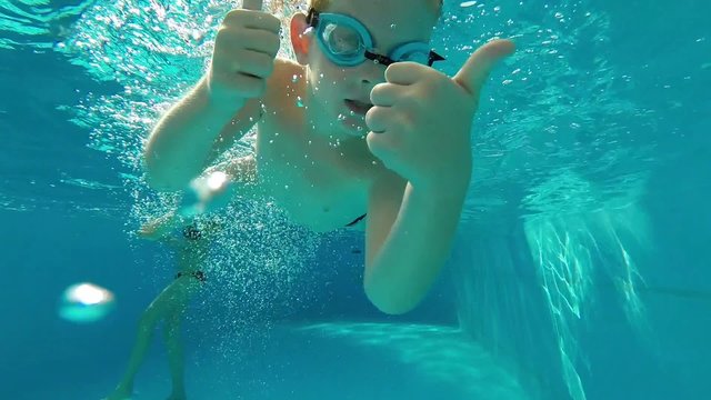 Young boy swimming under the water and show thumbs up and waving.