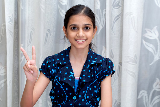 Young Indian Girl Showing Victory Sign With A Cute Smiling Face 