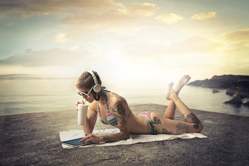 Tattooed girl with milkshake and tablet at the beach