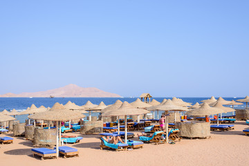 Fototapeta premium Thatched beach umbrellas and recliner chairs