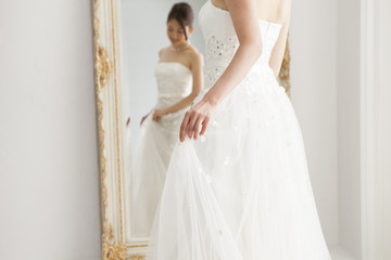 Fototapeta premium Woman wearing a wedding dress is looking in the mirror in the dressing room