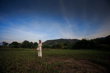 blonde girl in Vietnamese dress with hat in hand on field