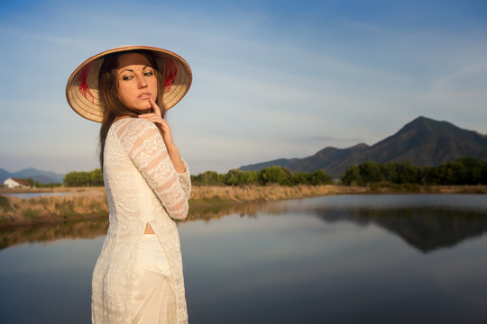 Portrait Of Girl In Vietnamese Hat Against Country Lakes