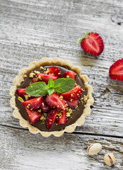tartlet with chocolate cream, strawberries and pistachios on a light wooden background