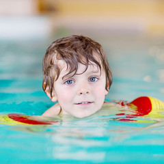 Fototapeta na wymiar little kid boy with swimmies learning to swim in an indoor pool