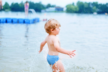 Little blond kid boy having fun with splashing in a lake, outdoo