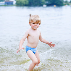 Little blond kid boy having fun with splashing in a lake, outdoo