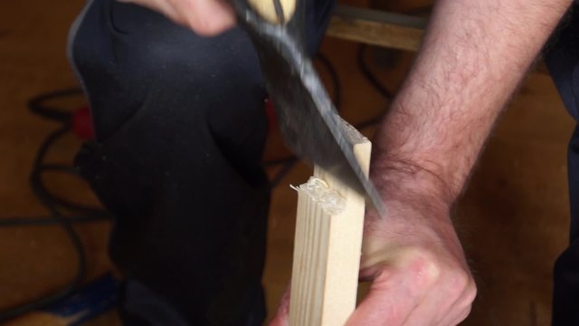 Man cleaves pieces of wood from the board using ax indoors
