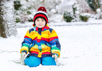 Funny preschool boy in colorful clothes happy about snow, outdoo