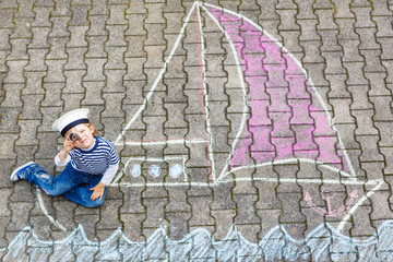 Little kid boy having fun with ship picture drawing with chalk