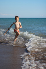 Fototapeta premium War with waves. boy with wooden sword playing in the waves at the seaside