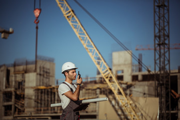 Engineer builder using a walkie talkie giving instructions at construction site.