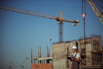 Engineer builder using tablet and walkie talkie, giving instructions at a construction site