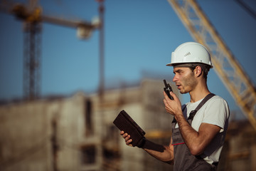 Engineer builder using a walkie talkie giving instructions at construction site.