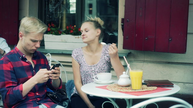 Girl eating mousse from coffee and boy using smartphone in the cafe
