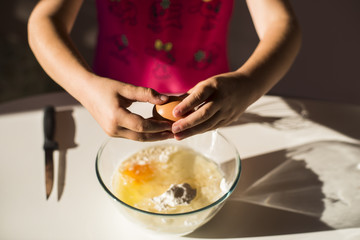 Obraz na płótnie Canvas Hands of preteen girl breaking egg into flour in transparent bowl