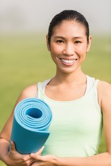 Smiling sporty woman holding exercise mat