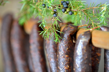 Dunkel geräucherte Südtiroler Kaminwurzen zur Trocknung aufgehängt, frischer Wacholder als Deko
