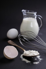 eggs, flour, milk and whisk on a dark background