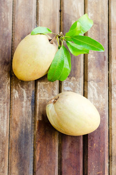 Fresh sweet sapodilla fruit with leaves on wooden background