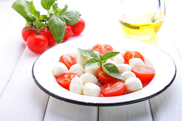 red tomatoes, garlic, basil and mozzarella cheese on a white wooden background