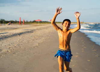 Happy boy running on the sea beach at summer.
