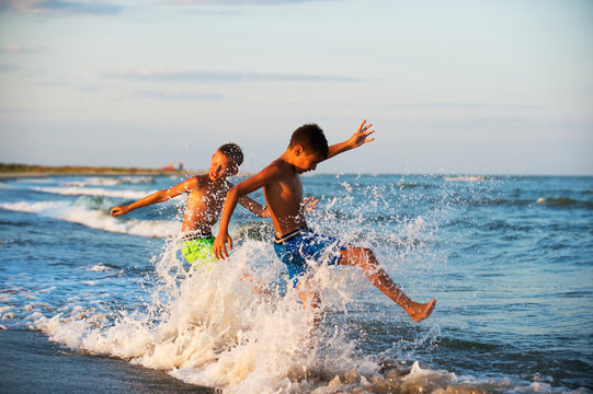 Two boys adolescence playing in the sea water splashing feet wat