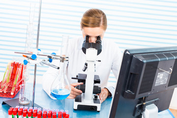 Fototapeta premium Woman in a medical lab technician with a microscope and a monito