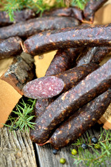 Originale dunkel geräucherte Südtiroler Kaminwurzen vor Holzscheite mit frischem Wacholder platziert 