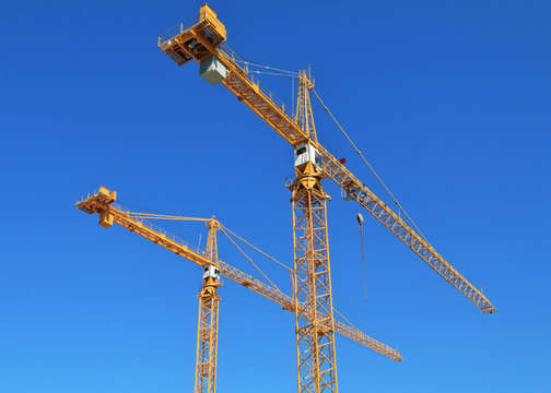 Two construction cranes against blue sky.