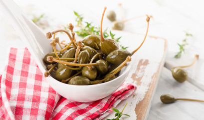 Pikled capers in a white spoon.