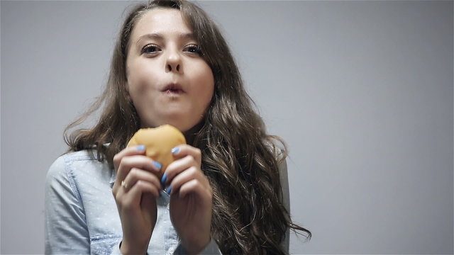 Young woman eating burger at gray background