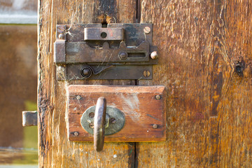The backside of an old door with a very old metal lock and some spiwe web