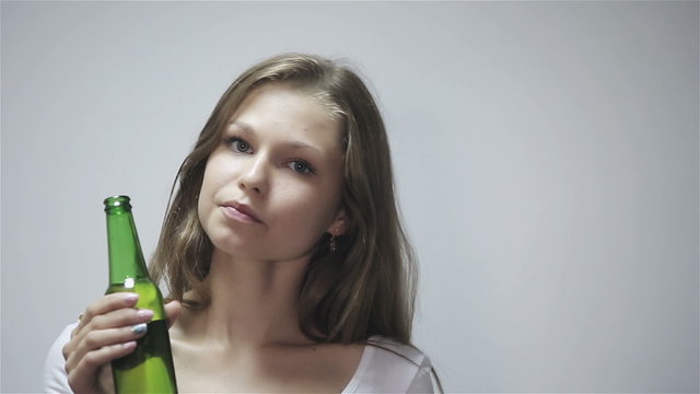 Young woman drinking beer at gray background