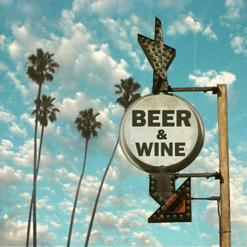 Aged and worn vintage photo of beer sign on beach with palm trees