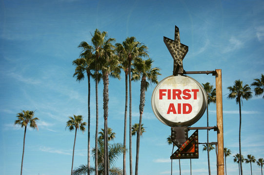 aged and worn vintage photo of first aid sign on beach with palm trees