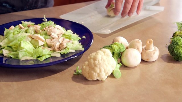 Man preparing dinner salad cutting lettuce and fresh vegetables with a knife