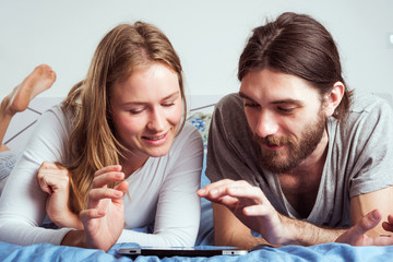 young caucasian couple using tablet in bed