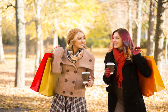 Two beautiful women having a relaxing conversation with coffee after shopping walking in the autumn park.