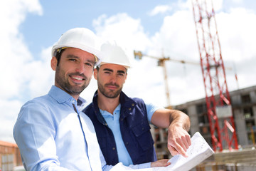 Engineer and worker watching blueprint on construction site