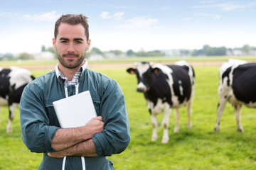 Portrait of a young attractive farmer in a pasture with cows - obrazy, fototapety, plakaty