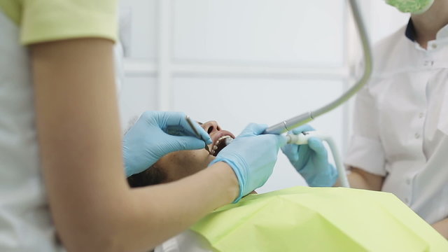 Young african american woman patient in the dental clinic on treatment. Hands of dentist and assistant during visit of customer