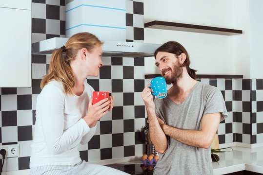 Young Happy Smiling Caucasian Couple On Kitchen Drinking Morning Coffee And Talking To Each Other