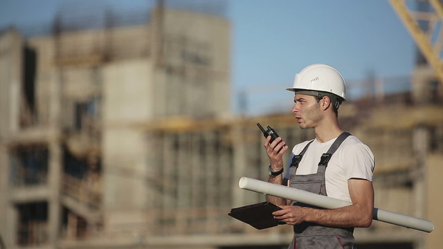 Engineer builder using tablet and walkie talkie, giving instructions at a construction site