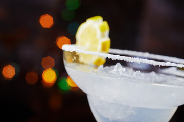 bright refreshing cocktail daiquiri on a table in a restaurant with creative decoration of orange slices and ice on a wooden table in a bar with a beautiful dance disco lights bokeh in the background.