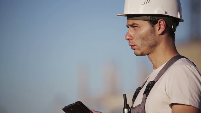 Engineer builder using tablet and walkie talkie, giving instructions at a construction site. Close up