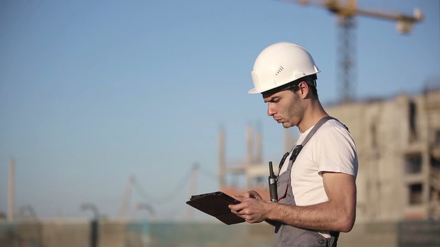 Engineer builder using tablet and walkie talkie, giving instructions at a construction site