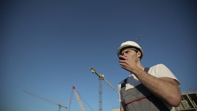 Engineer builder using a walkie talkie giving instructions at construction site. Slow motion
