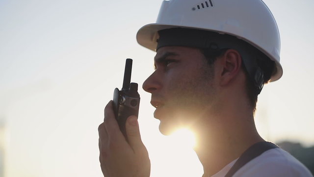 Engineer builder using a walkie talkie giving instructions at a construction site. Sunset time