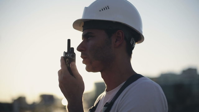 Engineer builder using a walkie talkie giving instructions at a construction site. Sunset time
